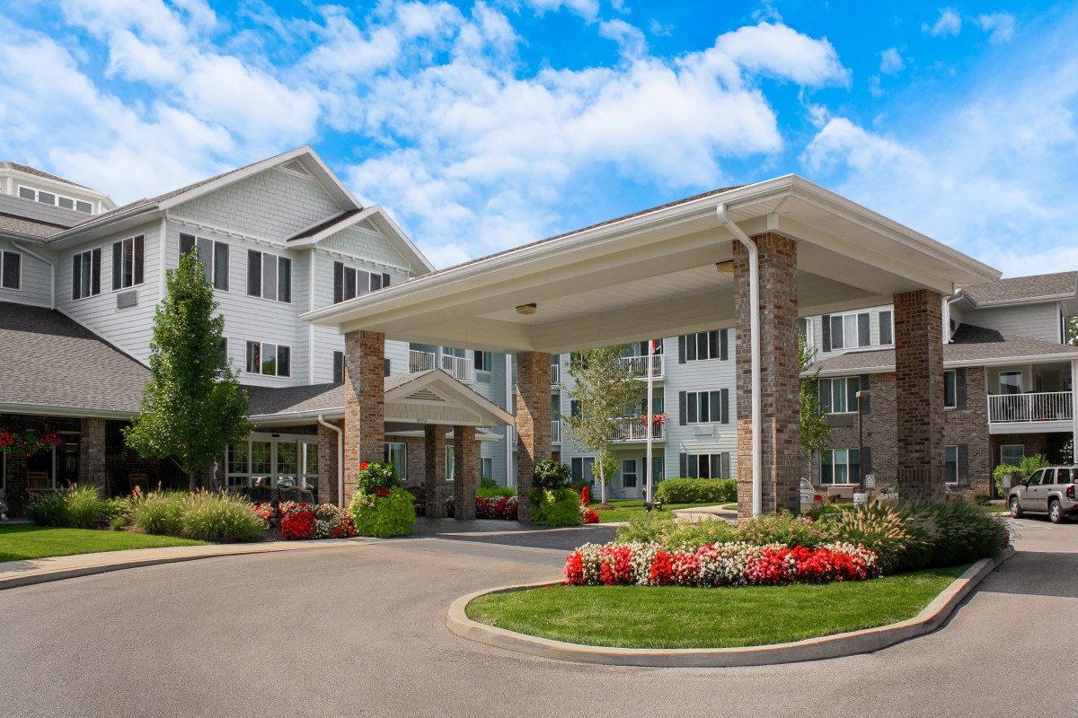 A well-maintained residential building with a landscaped entrance and vibrant flowers under a bright, cloudy sky.