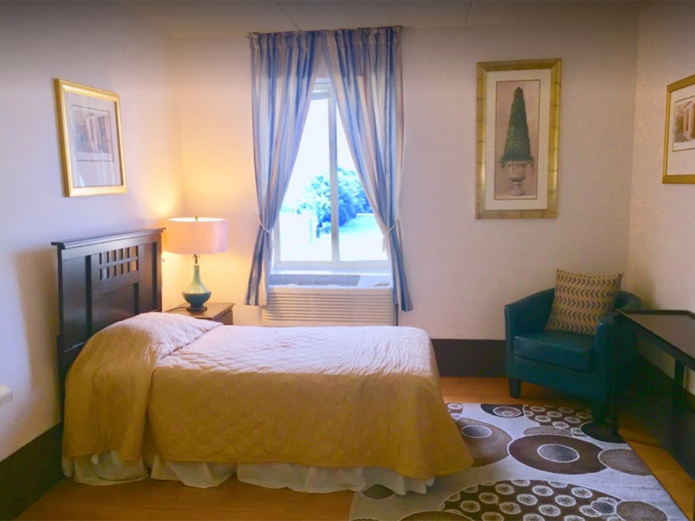 A cozy bedroom with a single bed, bedside lamp, and decorative artwork.