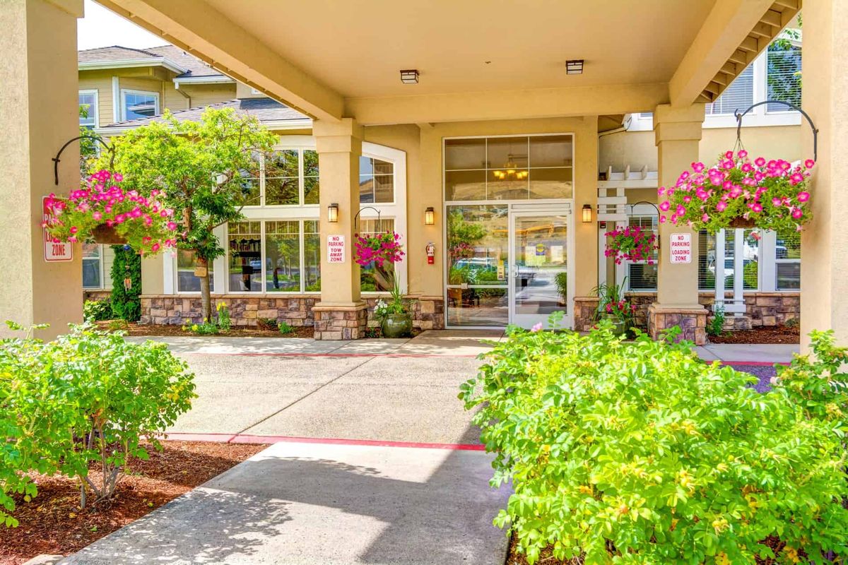 A well-maintained building entrance with glass doors, surrounded by lush greenery and columns.