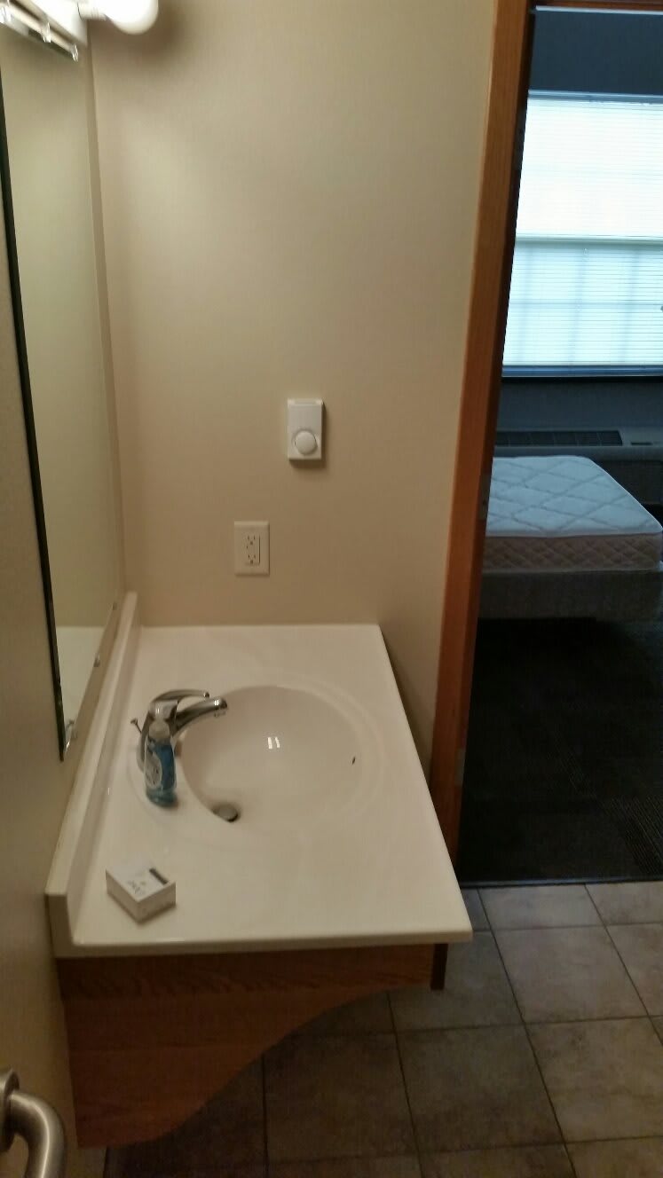 A view of a bathroom sink with a mirror, adjacent to a bedroom.