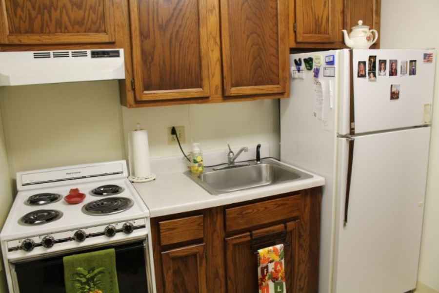 A compact kitchen setup featuring a stove, sink, and refrigerator with wooden cabinets.