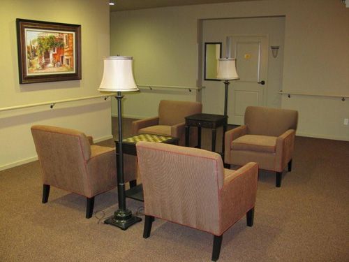 A cozy waiting area with four chairs, two lamps, and a central table on a carpeted floor.