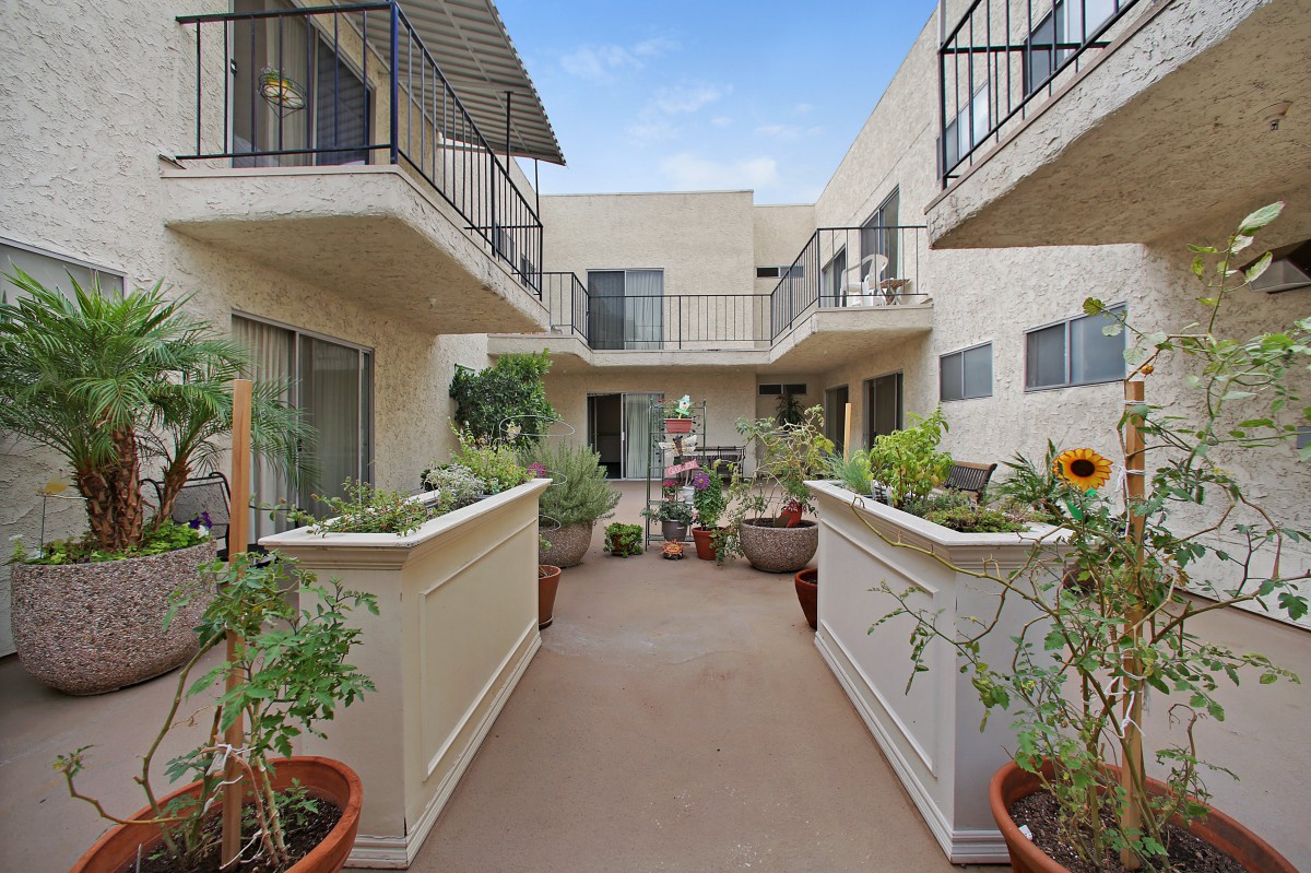 A modern apartment complex with balconies and a walkway adorned with plants.