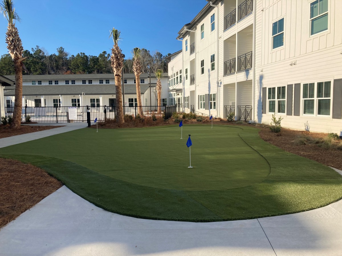 A residential building with an outdoor putting green surrounded by landscaped areas.