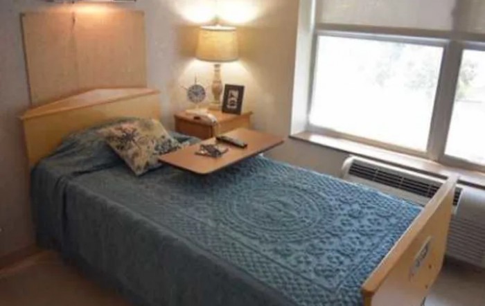 A cozy bedroom with a neatly made bed, nightstand, and lamp by the window.