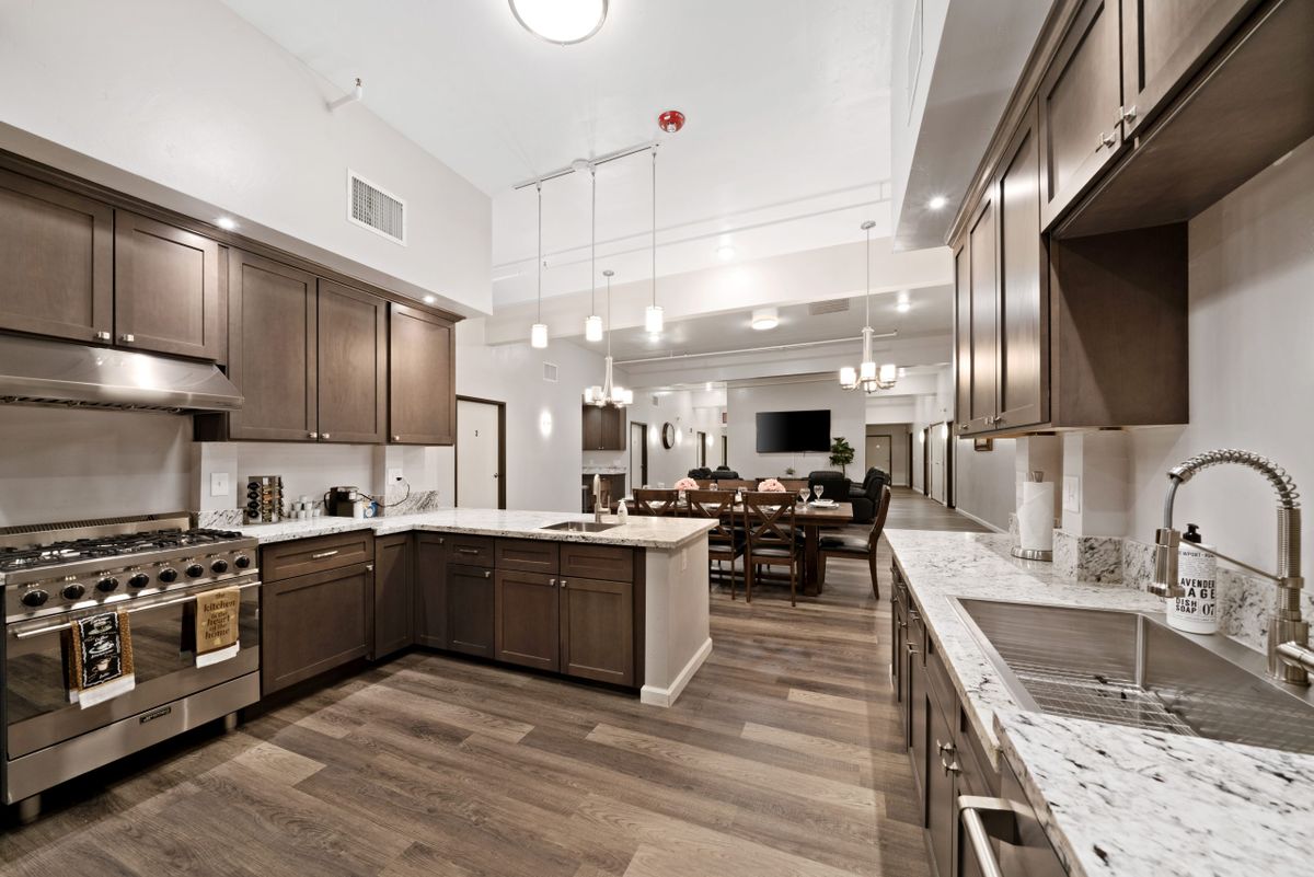 A modern kitchen with wooden cabinets and marble countertops, featuring an open layout and bright lighting.