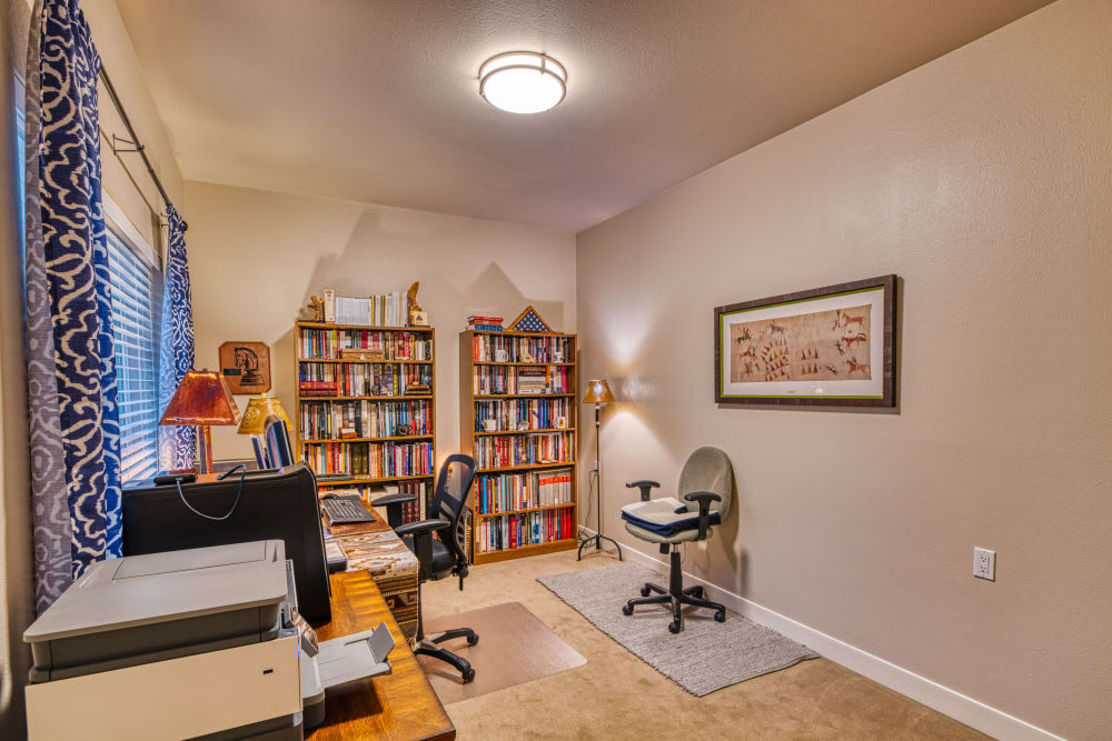 A cozy home office featuring bookshelves filled with books, a desk with a computer chair, and decorative artwork on the wall.