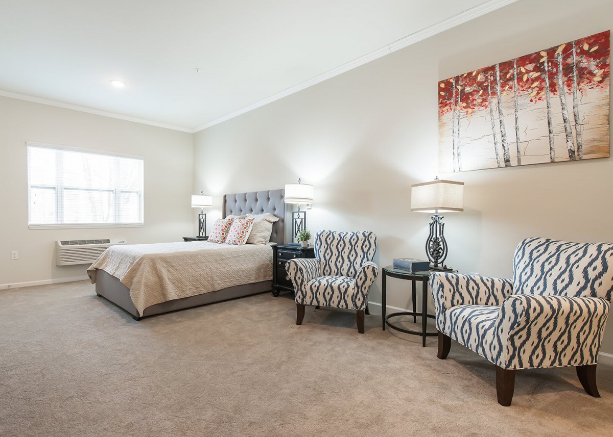 A modern bedroom with a large bed, decorative armchairs, and stylish lamps.