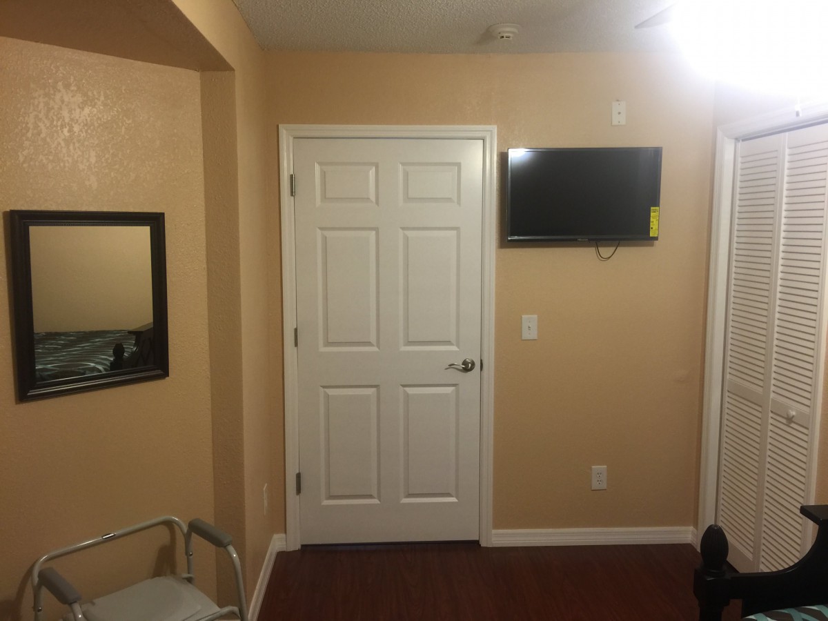 A simple room interior with a door, wall-mounted television, and a mirror.