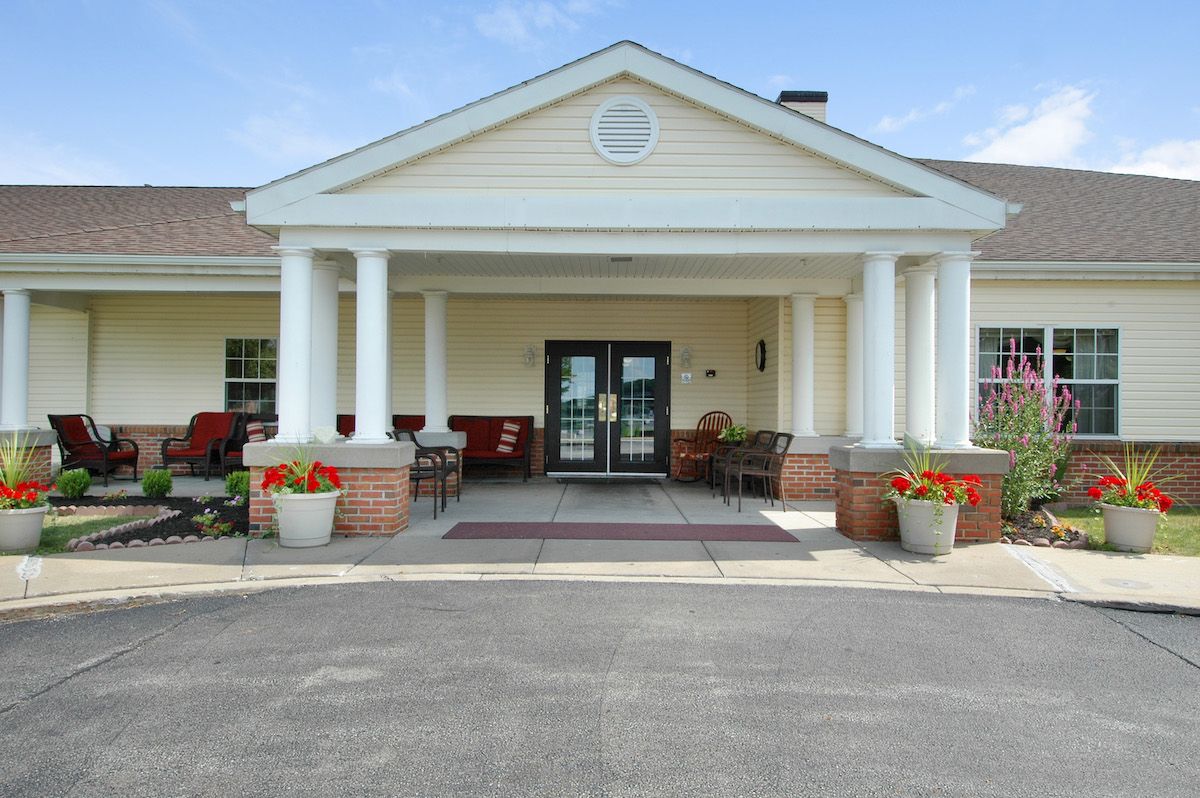 A building entrance with white columns and a porch decorated with red flowers.