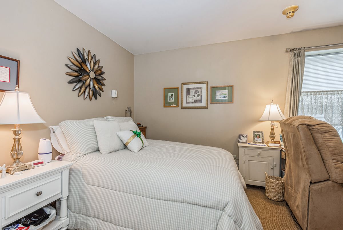 A cozy bedroom with a neatly made bed, decorative wall art, and a lamp on the nightstand.