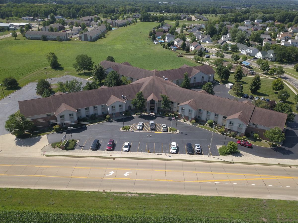 Aerial view of a large building with a parking lot, surrounded by residential homes and greenery.