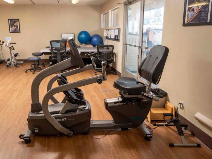 A small gym featuring a stationary exercise bike and office area in the background.