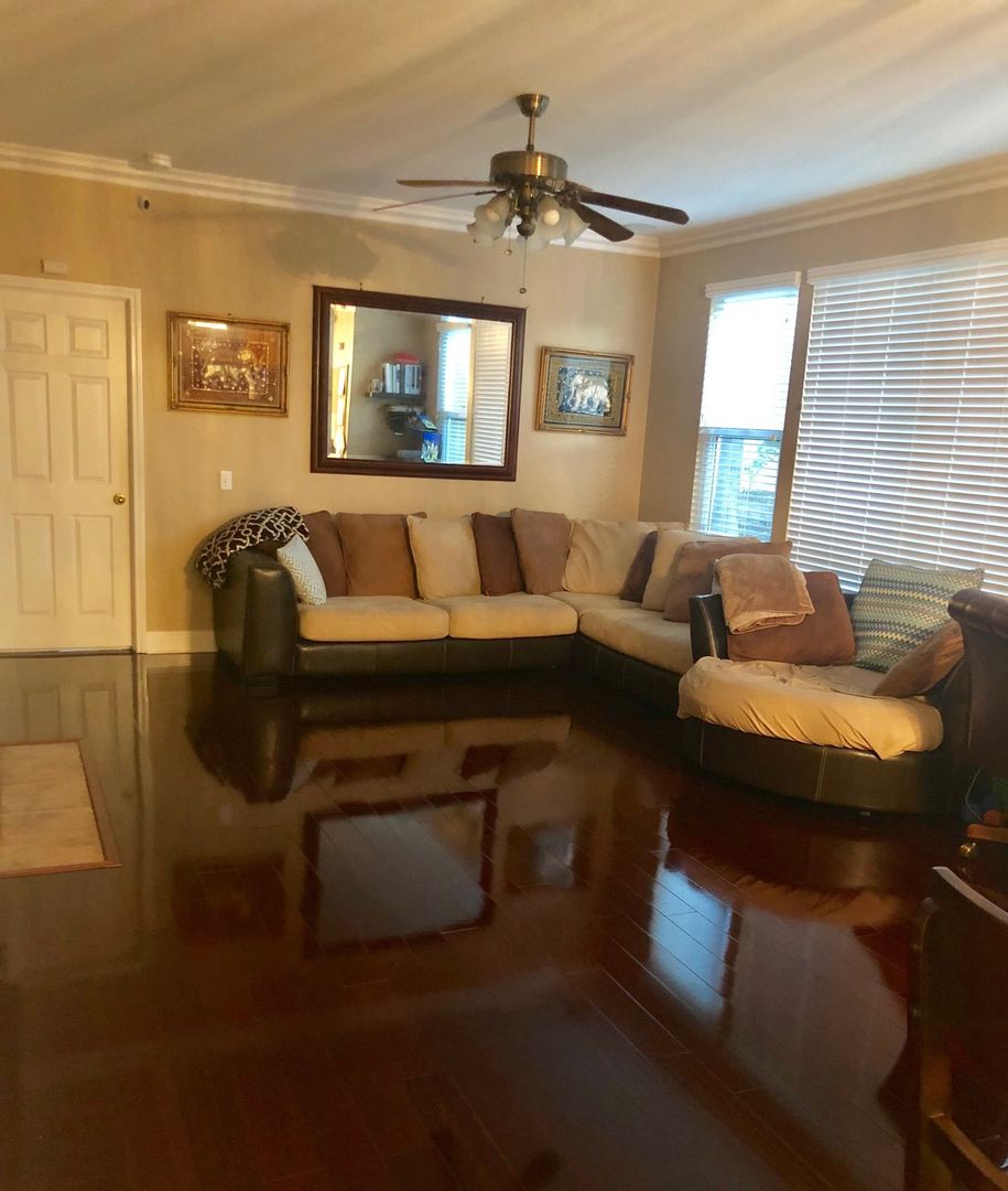 A cozy living room with a large sofa, hardwood flooring, and a ceiling fan.