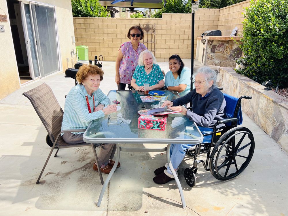 A group of seniors and caregivers enjoying time together outdoors around a table.
