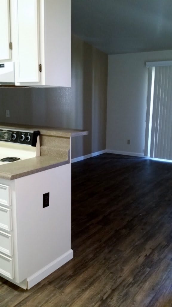 An empty apartment interior with a kitchen area and hardwood floors.