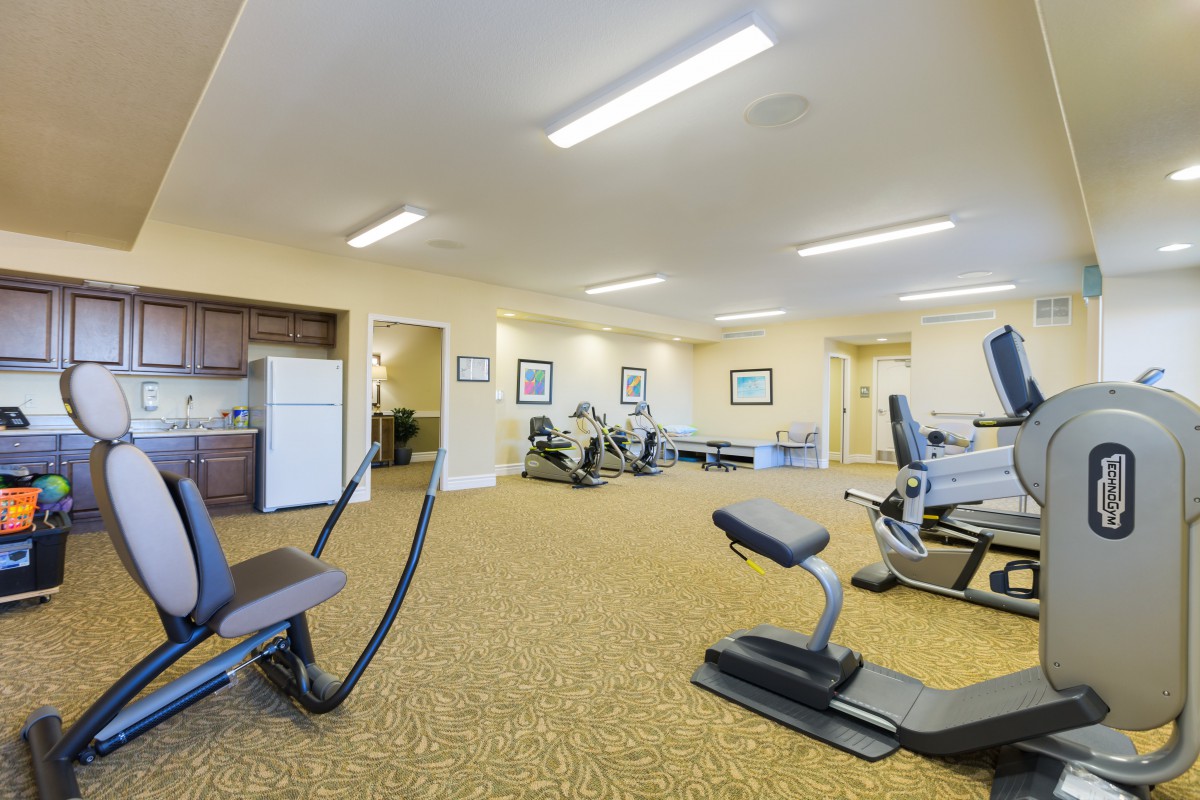 A spacious gym with various exercise equipment and bright lighting.