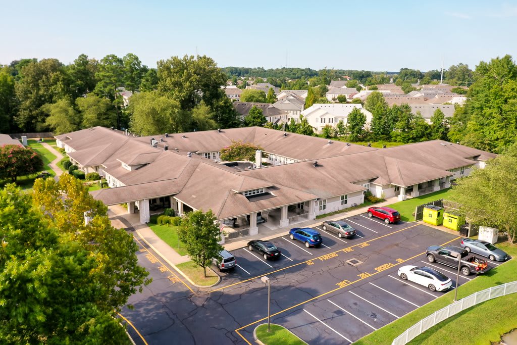 Aerial view of a suburban building with a parking lot surrounded by trees and residential homes.