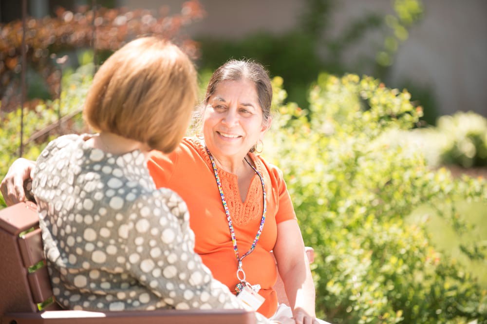 Two women sitting and talking in a sunny garden.