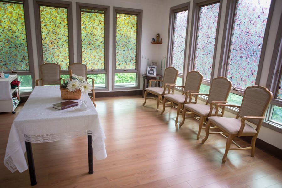 A serene, light-filled room with elegant chairs lined up against the walls and a table adorned with flowers.