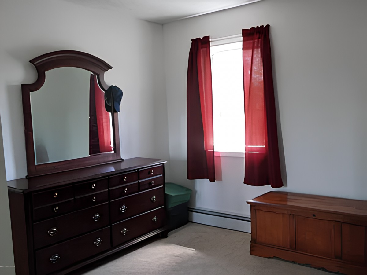 A bedroom with a dresser and mirror, red curtains, and a wooden chest.
