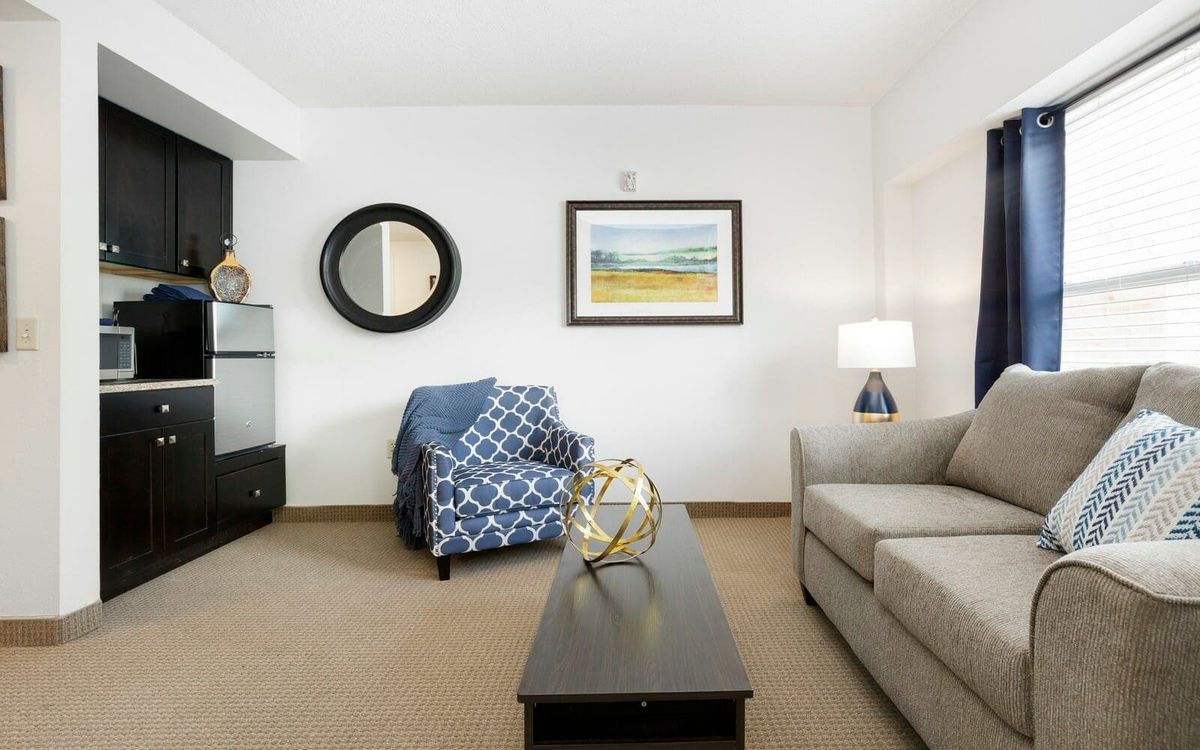 A cozy living room with a sofa, armchair, and coffee table, decorated with wall art and a mirror.