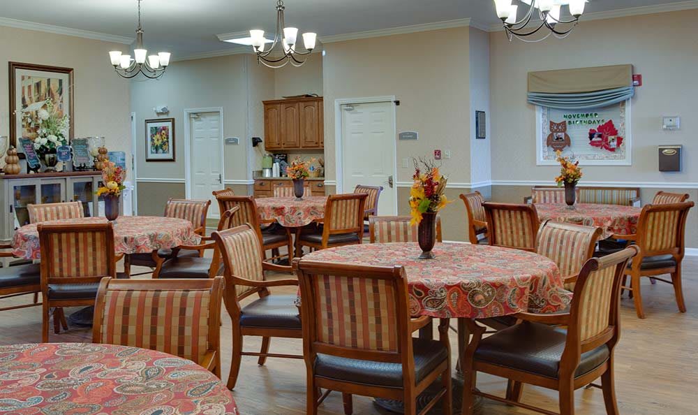 An empty dining room with round tables and chairs, decorated with floral tablecloths and vases of flowers.