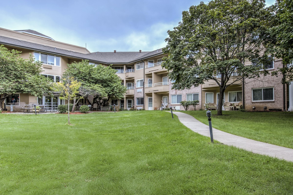 A residential apartment building with a well-maintained lawn and surrounding trees.