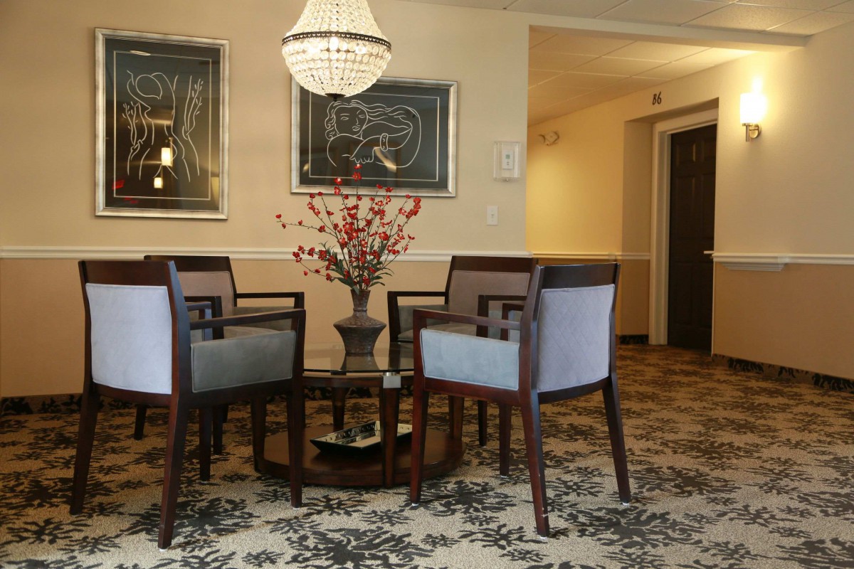 A cozy living room area with elegant chairs and a table, decorated with a chandelier and artwork on the walls.