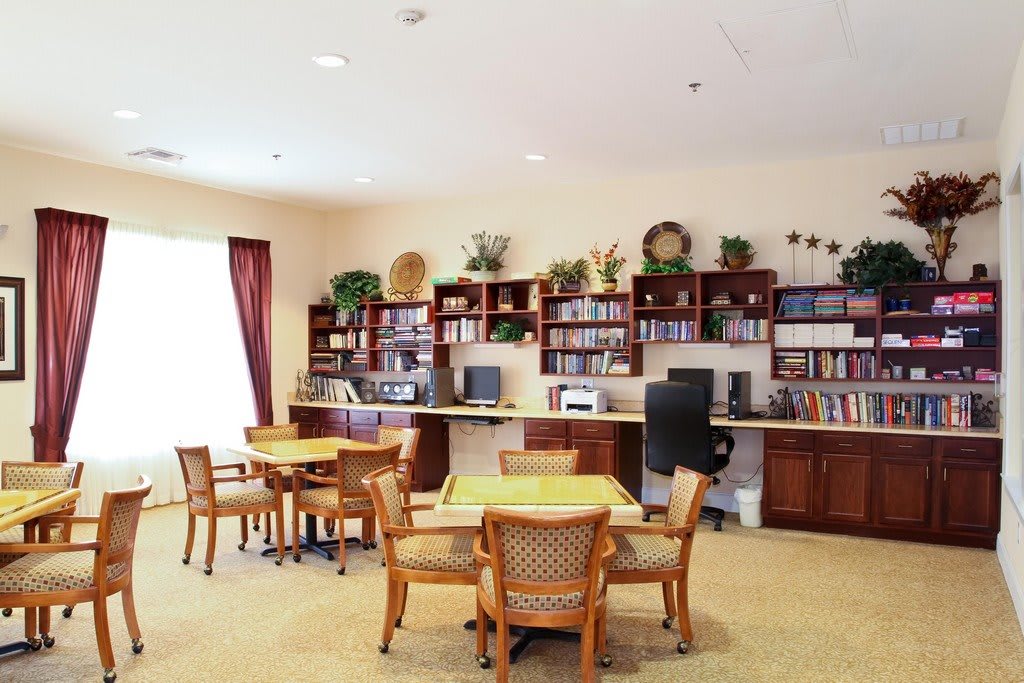 A cozy library interior with tables, chairs, and bookshelves filled with books and decorative items.