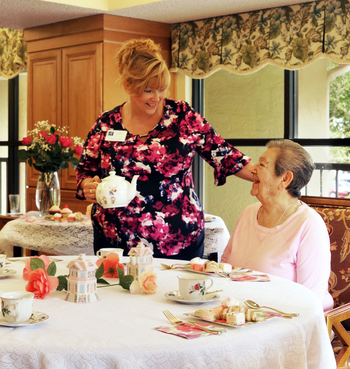 A caregiver is serving tea to an elderly woman at a social gathering.