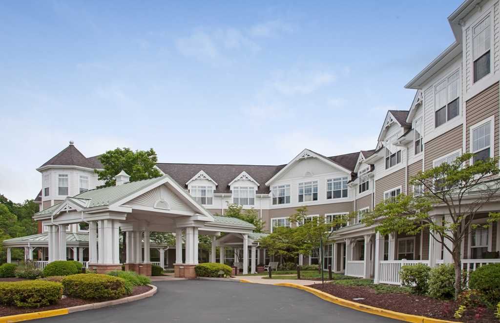 A white, multi-story residential building with landscaped surroundings and a welcoming entrance.