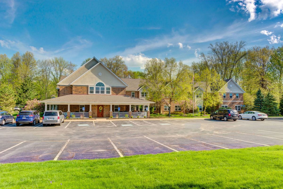 A parking lot in front of a large building surrounded by trees on a sunny day.