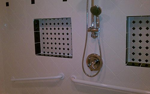 A bathroom shower with a handheld showerhead, tiled wall niche, and grab bars.