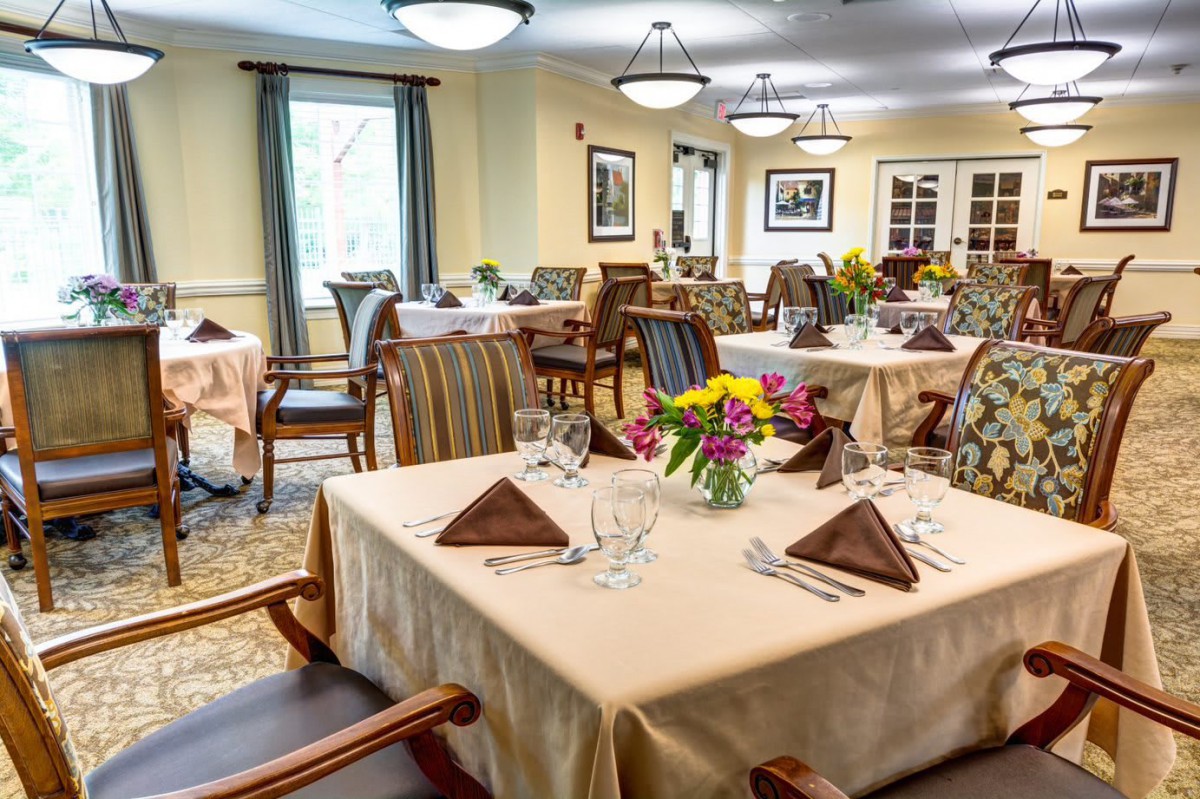 An elegant dining room with neatly arranged tables, featuring floral centerpieces and folded napkins.