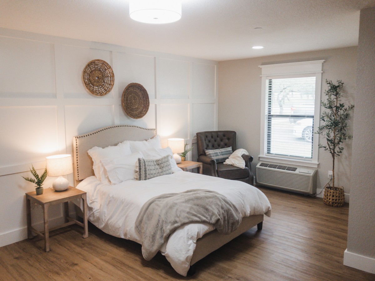 A cozy and modern bedroom with neutral tones, featuring a comfortable bed, decorative pillows, wooden flooring, and ambient lighting.