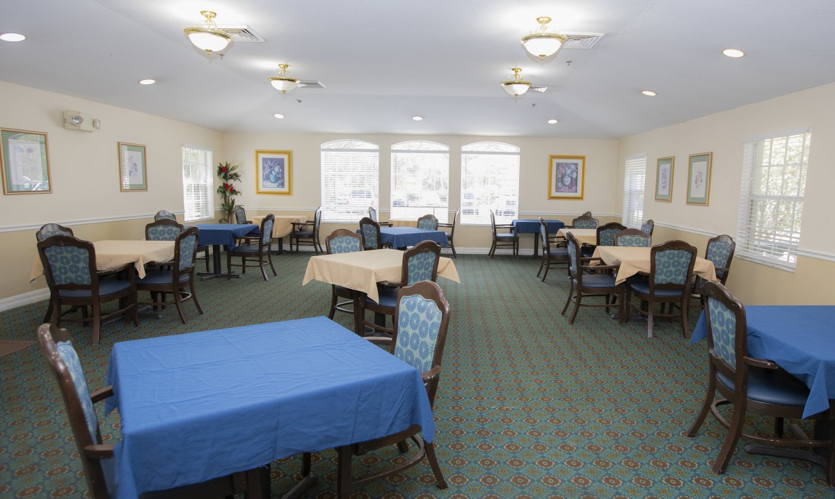 A spacious dining area with multiple tables and chairs, featuring large windows and framed artwork on the walls.