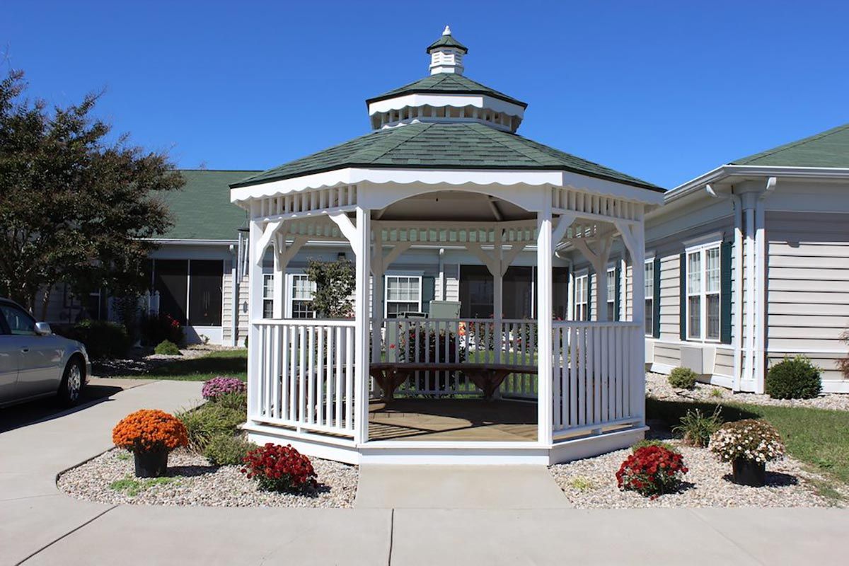 A white gazebo with a green roof surrounded by flowers and a paved path.