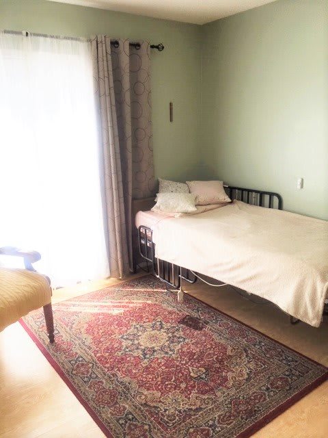 A simple bedroom with a single bed and natural light streaming through the window.