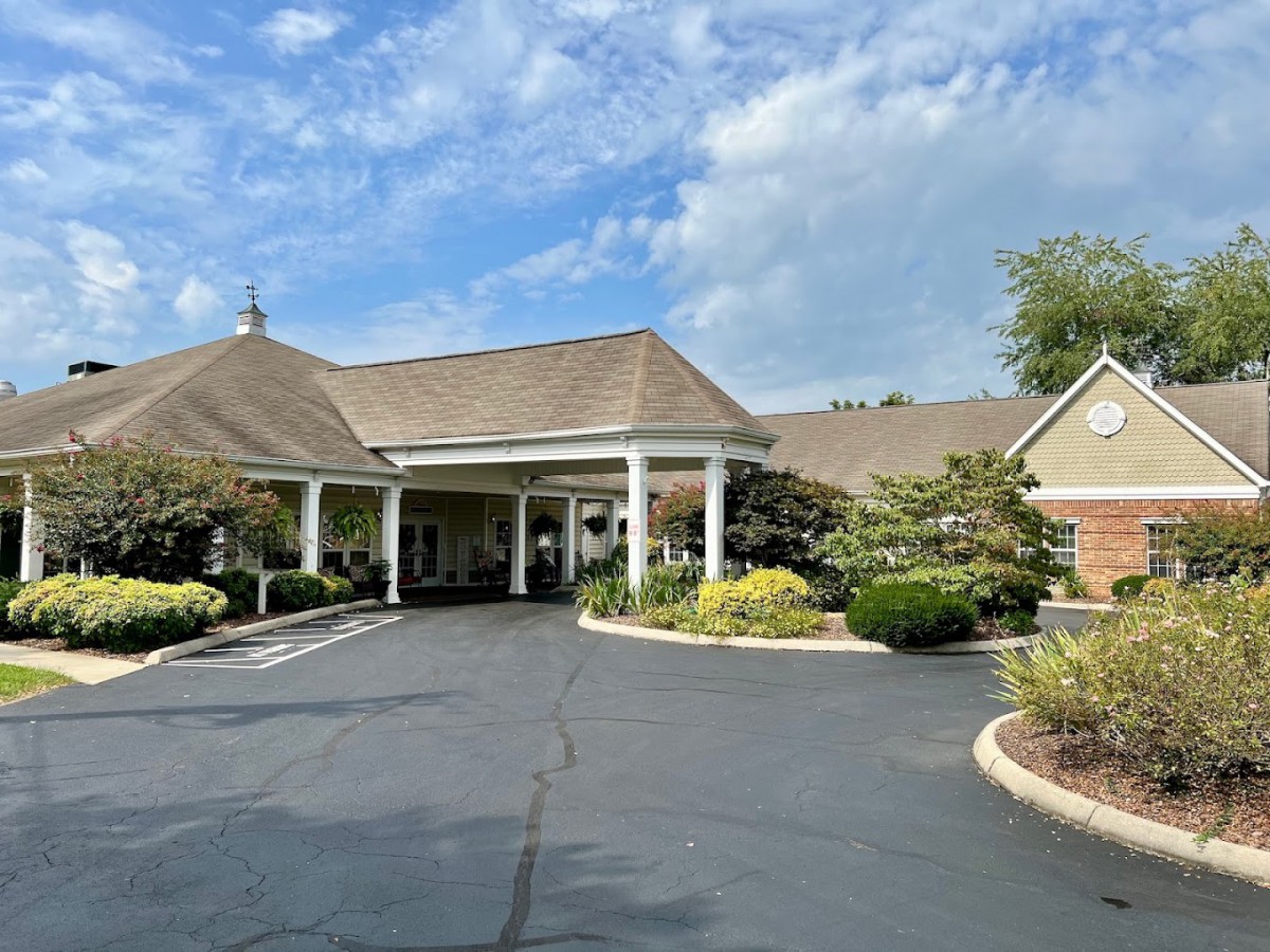 A scenic view of a building entrance with a driveway surrounded by lush greenery and a partly cloudy sky.