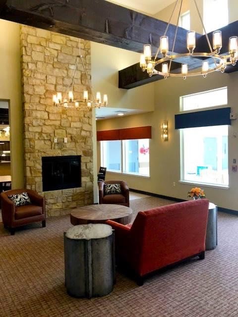 A cozy lounge with a stone fireplace, comfortable seating, and a modern chandelier.