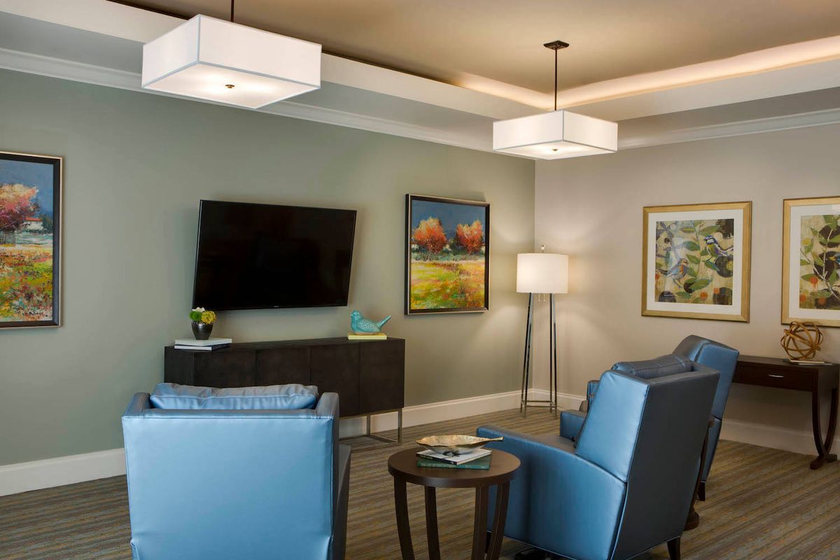 A modern living room with blue chairs, wall-mounted television, and colorful artwork.