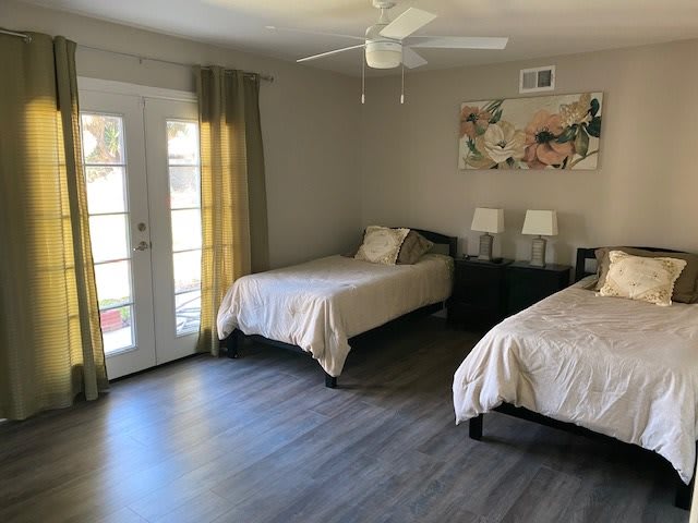 A modern bedroom with twin beds, featuring laminate flooring and natural light from the French doors.