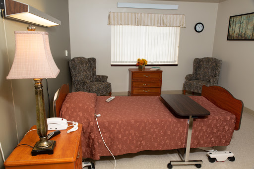 A well-furnished hospital room featuring a bed, seating area, and natural light.