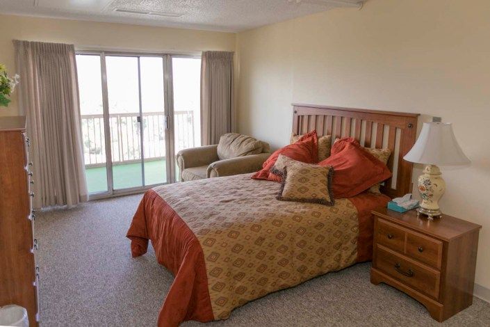 A cozy bedroom featuring a bed with a patterned comforter, a chair by the window, and access to a balcony.