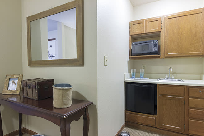 Compact kitchen area with wooden cabinets, a microwave, and a sink adjacent to a small table and mirror.