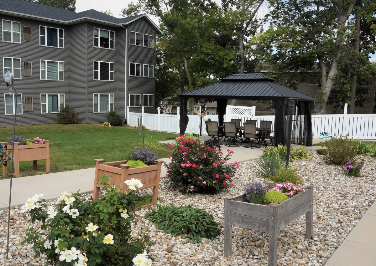 A landscaped garden area with colorful flowers and a gazebo, situated near an apartment building.