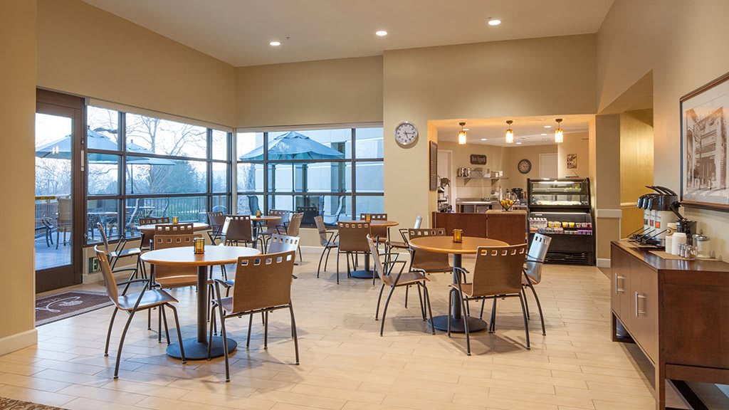 An empty cafe interior with tables and chairs, featuring large windows allowing natural light.