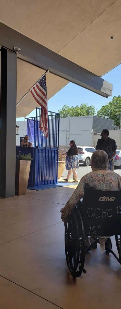 People are gathered in an outdoor waiting area, with one person in a wheelchair.