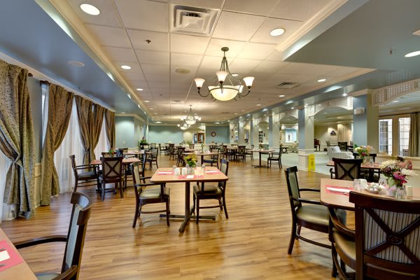 An elegant dining room with neatly arranged tables and chairs, illuminated by chandeliers.